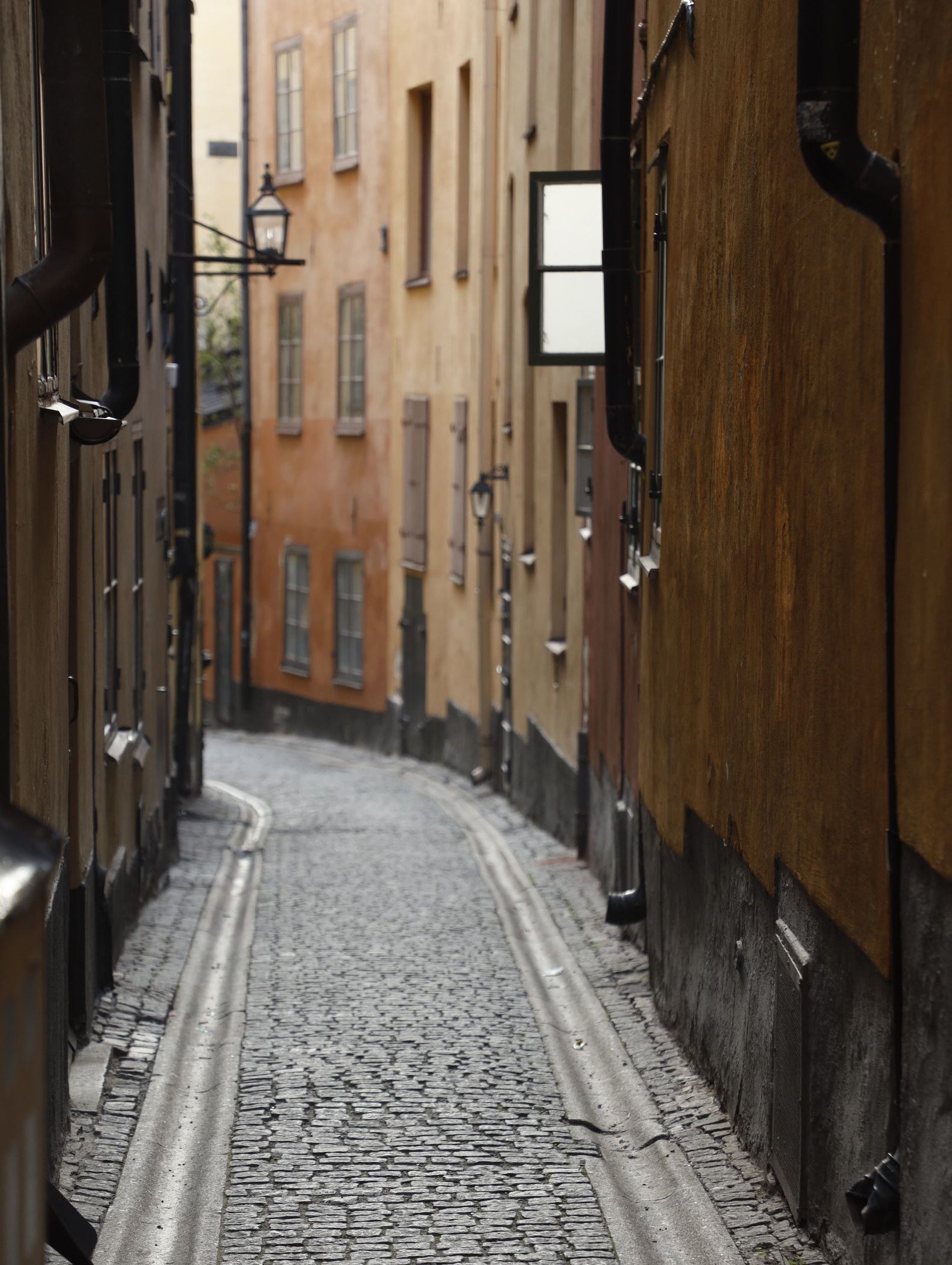En tom kullerstensgränd i gamla stan. De brunröda husen står tätt.
